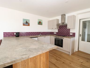 A kitchen with purple tile backsplash gray cabinets and wooden floor at Waveney View Cottage in Burgh Castle