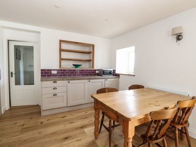 A kitchen with wooden dining table and chairs beside cabinets with purple tile backsplash at Waveney View Cottage in Burgh Castle