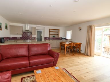 An open living area with a red leather sofa wooden dining table and kitchen cabinets at Waveney View Cottage in Burgh Castle