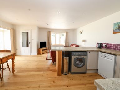 An open plan kitchen and living area with wooden floor a washing machine dishwasher and a wooden table at Waveney View Cottage in Burgh Castle