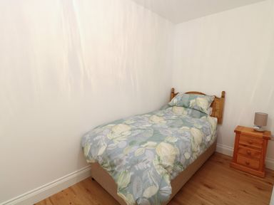 A single bed with floral bedding and a wooden headboard next to a wooden nightstand with a lamp on it in a bedroom at Waveney View Cottage in Burgh Castle