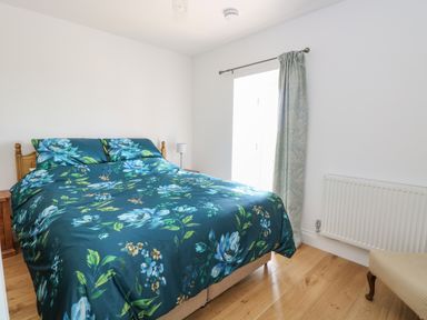 A bedroom with a wooden bed with floral bedding beside a window with a curtain and a radiator at Waveney View Cottage in Burgh Castle