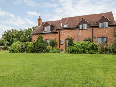 A brick cottage with dormer windows surrounded by bushes and a green lawn at Lawn Farm Cottage in Churcham near Gloucester