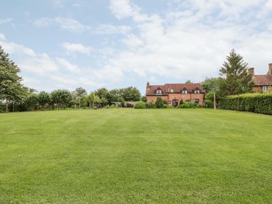 A large grassy lawn with trees and bushes and a brick house in the background at Lawn Farm Cottage Churcham near Gloucester
