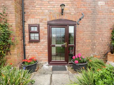 A front door with glass panels set in a brick wall with two small windows and potted plants on either side at Lawn Farm Cottage in Churcham near Gloucester
