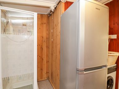 A laundry room with a silver refrigerator a washing machine a shower and wooden panel walls at Lawn Farm Cottage in Churcham near Gloucester