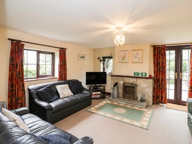 A living room with black leather sofas a fireplace and a television at Lawn Farm Cottage in Churcham near Gloucester