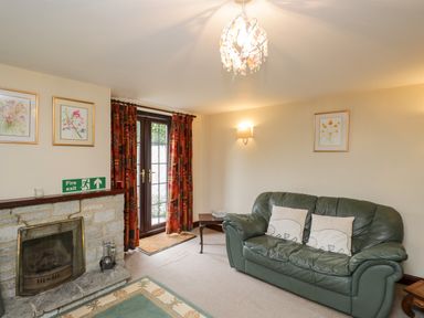 A living room with a green leather sofa pillows on the sofa a stone fireplace and glass doors with patterned curtains at Lawn Farm Cottage in Churcham near Gloucester