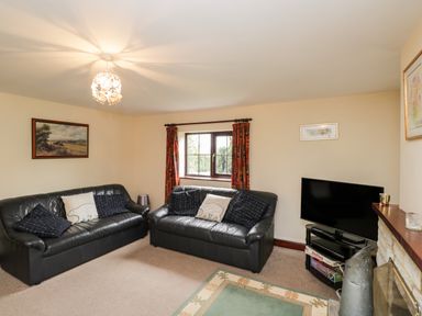 A living room with two black leather sofas a window with red curtains a television and a stone fireplace at Lawn Farm Cottage Churcham near Gloucester