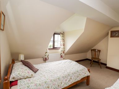 A bedroom with a single bed floral bedding a wooden chair and a window with floral curtains at Lawn Farm Cottage in Churcham near Gloucester