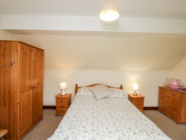 A bedroom with a bed between two nightstands with lamps a wooden wardrobe and a wooden dresser with a pink pitcher and bowl on top at Lawn Farm Cottage in Churcham near Gloucester