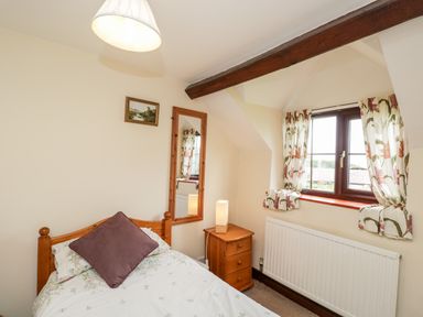 A small bedroom with a single bed a bedside table with a lamp a window with floral curtains and a mirror on the wall at Lawn Farm Cottage Churcham near Gloucester