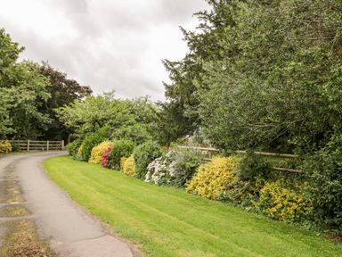 A garden path next to a lawn and a flower bed with bushes and trees at Lawn Farm Cottage in Churcham near Gloucester