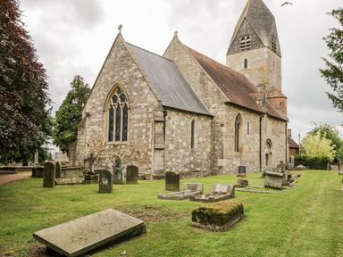An old stone church with stained glass windows and a graveyard with tombstones on grass