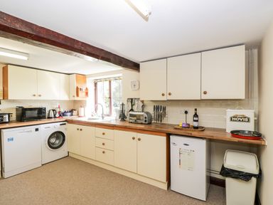 A kitchen with white cabinets wooden countertops a washing machine a microwave a toaster and a small refrigerator at Lawn Farm Cottage in Churcham near Gloucester