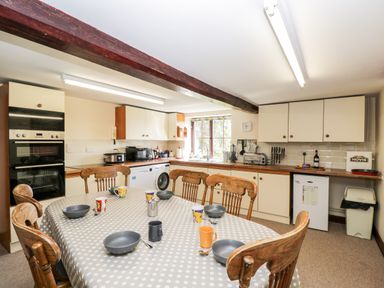 A kitchen with wooden chairs around a dining table with polka dot tablecloth and bowls cups at Lawn Farm Cottage in Churcham near Gloucester