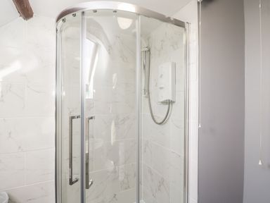 A bathroom with a glass enclosed corner shower and white marble tiled walls at Lawn Farm Cottage in Churcham near Gloucester