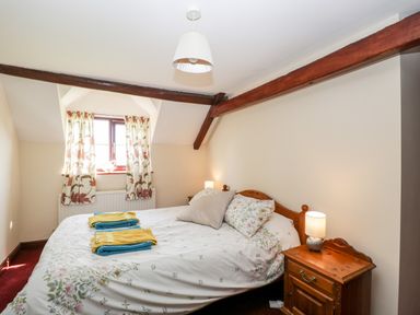 A bedroom with a double bed bedside tables lamps floral curtains and wooden ceiling beams at Lawn Farm Cottage in Churcham near Gloucester