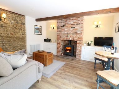 A living room with a wood burning stove and brick fireplace at Captain's Cottage in Sheringham