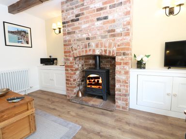 A living room with a wood-burning stove in a brick fireplace flanked by white cabinets at Captains Cottage in Sheringham