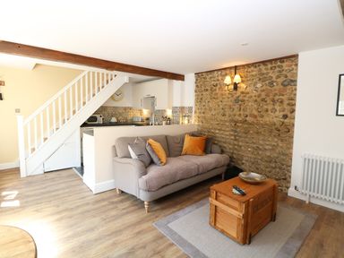 A living room with a sofa and coffee table next to a small kitchen and staircase at Captains Cottage in Sheringham