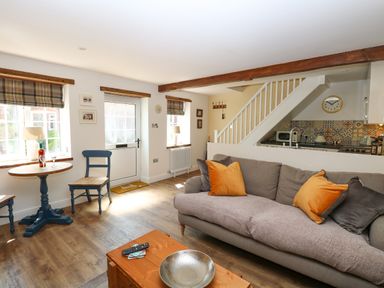 A living room with a sofa and orange cushions a wooden coffee table and a small dining table with chairs at Captain's Cottage in Sheringham