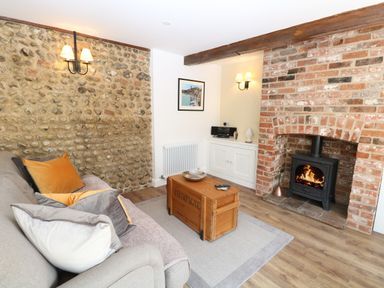 A living room with a stone wall, sofa with cushions, wooden coffee table, brick fireplace with a stove at Captains Cottage in Sheringham