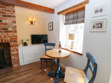 A small dining area with a round wooden table two chairs a window with a lamp on the sill and a television on a cabinet at Captains Cottage in Sheringham
