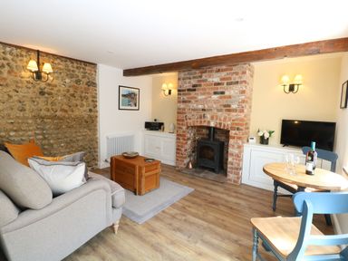 A living room with a stone and brick fireplace a sofa wooden floor and a small dining table at Captains Cottage in Sheringham