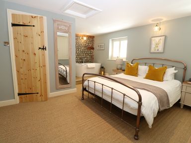 A bedroom with a metal bed frame with mustard pillows a bathtub beside a stone wall and a full length mirror at Captain's Cottage in Sheringham
