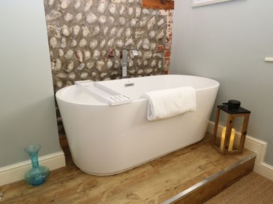 A white freestanding bathtub with a towel on the edge and a wooden lantern with a candle beside it at Captain's Cottage in Sheringham