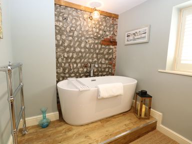 A bathroom with a freestanding bathtub against a stone wall at Captains Cottage in Sheringham