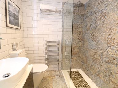 A bathroom with a white sink, toilet, towel rack, and a shower with patterned tiles at Captain's Cottage in Sheringham