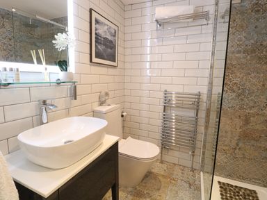 A bathroom with a sink, toilet, towel rack, shower area, and framed photo at Captains Cottage in Sheringham