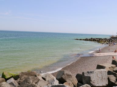 A pebble beach with people swimming and rocks along the shore at Captain's Cottage in Sheringham