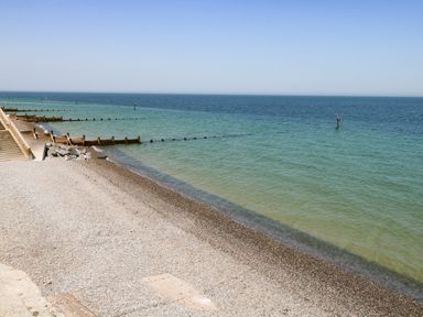 A pebble beach with steps leading down to it and groynes extending into the sea at Captains Cottage in Sheringham