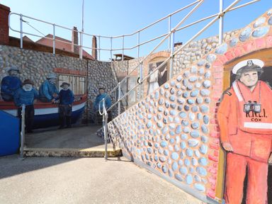 A painted stone wall with railings and murals of fishermen and a lifeboat crew at Captain's Cottage in Sheringham