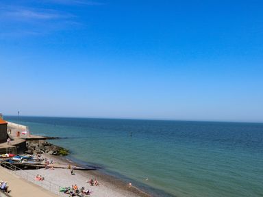 A pebble beach with people sunbathing and swimming near boats at Captain's Cottage in Sheringham