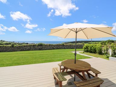 An outdoor patio with a round wooden table and umbrella overlooking a grassy yard and stone wall at Atlantic View in Germoe