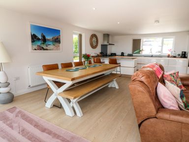 A dining area with a wooden table, bench, chairs, and a brown sofa in an open kitchen space at Atlantic View in Germoe