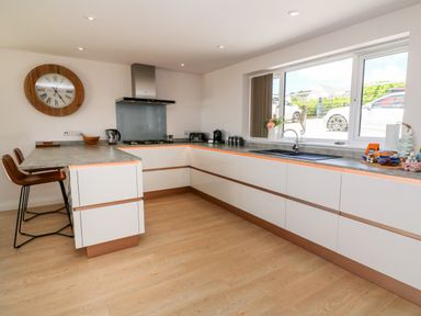 A kitchen with white cabinets a countertop stools a wall clock and a window at Atlantic View in Germoe