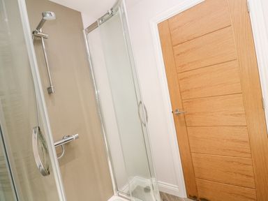A shower enclosure with sliding glass doors and a wooden door in a bathroom at Atlantic View in Germoe