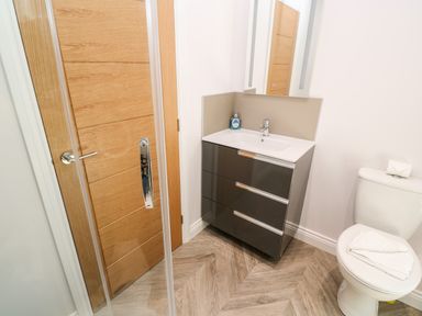A bathroom with a wooden door a modern sink cabinet a mirror and a toilet at Atlantic View in Germoe