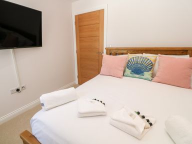 A bedroom with a wooden bed frame pillows on the bed towels and toiletries on the bed a wooden door and a wall-mounted television at Atlantic View in Germoe
