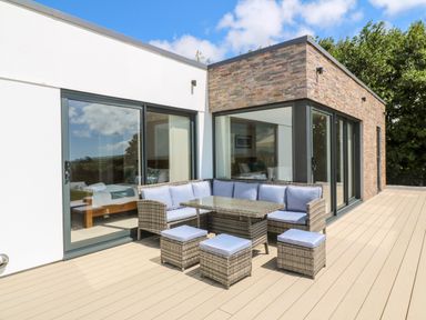 An outdoor patio with wicker seating and a glass table next to a modern building with sliding glass doors at Atlantic View in Germoe