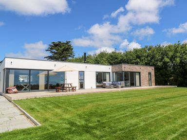 A modern single-story house with large glass windows a patio table with umbrella outdoor seating area and a lawn at Atlantic View in Germoe