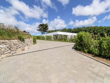 A paved driveway with stone wall and hedge leading to a single-story house surrounded by trees at Atlantic View in Germoe