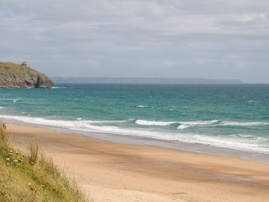 A sandy beach with waves and a cliff with a house on top at Atlantic View in Germoe