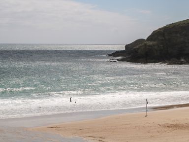 A beach with two people in the water and rocky cliffs at Atlantic View in Germoe