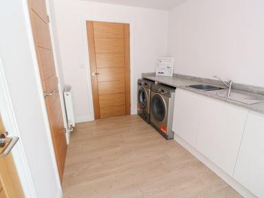A laundry room with washing machine dryer sink and wooden doors at Atlantic View in Germoe